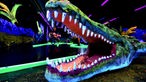 Das offene riesige Maul eines Krokodils in Neonfarben, Schwarzlicht