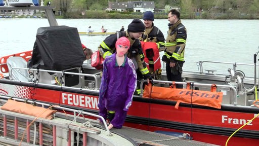 Eine Feuerwehrfrau steht auf einem Einsatzboot und hält die geborgene Sexpuppe in der Hand