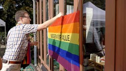 Ein Mann hängt eine Regenbogenflagge auf