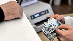 Mehrere Türkische Lira Scheine werden an einem Bankschalter an Kunden übergeben