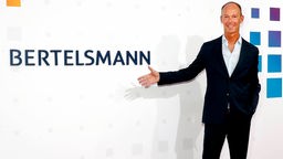 Bertelsmann-Chef Thomas Rabe lächelnd vor dem Schriftzug Bertelsmann