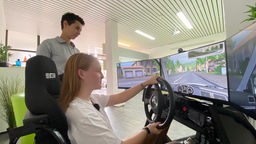 Fahrschülerin Zoey Vedder und Fahrschul-Angestellte Ela Titz gucken auf einen Fahrsimulator