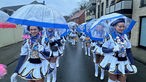 Eine Gruppe Frauen in weißen Kostümen mit blauen Regenschirmen