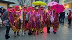 Menschen in bunten glitzernden Kostümen mit gelben und rosen Regenschirmen