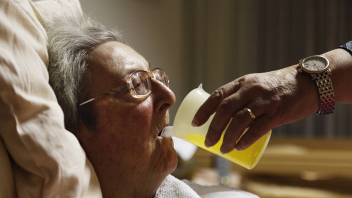 Altenpflegerin gibt einer Seniorin zu Trinken