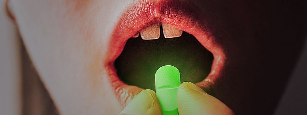 Eine leuchtende Pille wird vor einen Mund gehalten. 