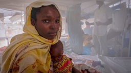 eine Mutter mit ihrtem unterernährten Kind in einem ärtzlichen Behandlungsraum.