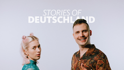 Die Hosts des Podcasts "Stories of Deutschland" Sina und Marius schütteln sich die Hände. Marius zeigt einen Daumen nach oben. 