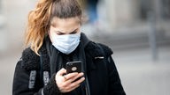Eine Frau mit Mundschutz hält ein Smartphone in der Hand