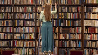 Frau auf einer Leiter vor einem Regal voller Bücher
