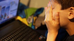 Dečak ispred laptopa drži ruke preko lica