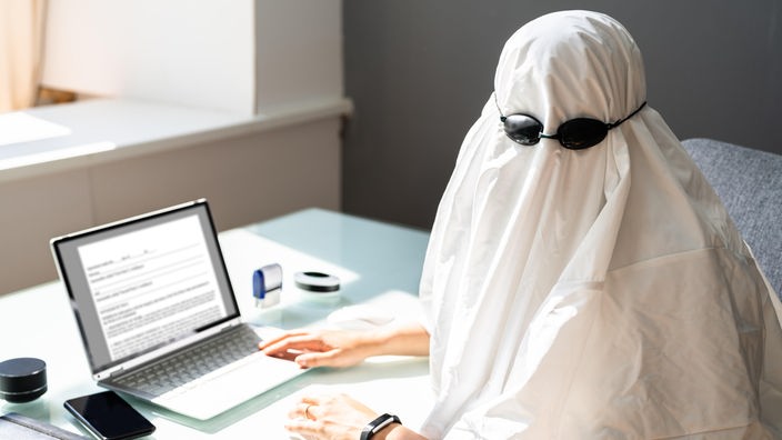osoba prekrivena belim čaršavom piše na laptopu