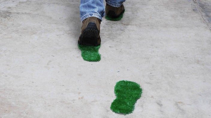Ilustracija: Čovek hoda po betonu, iza njega ostaju zeleni travnati otisci