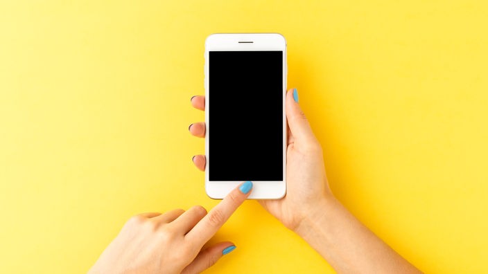 Ženske ruke drže beli smartfon na žutoj pozadini