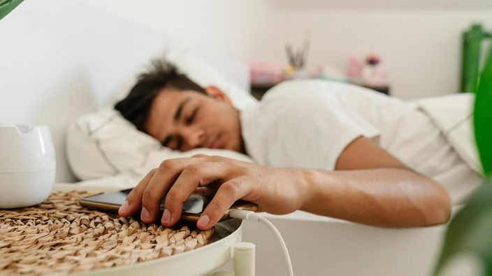 Čovek spava sa rukom na smartphonu
