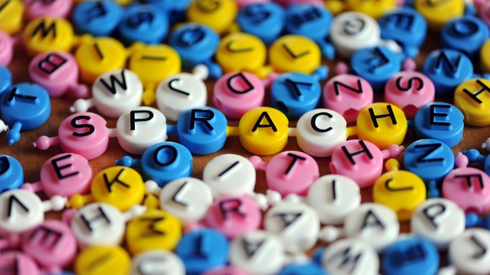 Reč "Sprache" (jezik), sastavljena od plastičnih slova iz porodične igrice, okolo mnogo drugih slova u različitim bojama