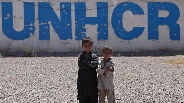 World Refugee Day: Zwei afghanische Jungen stehen vor einer Wand mit der Aufschrift UNHCR