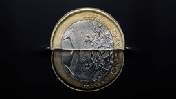 Eine Ein-Euro-Münze spiegelt sich in einer dunklen Flüssigkeit.