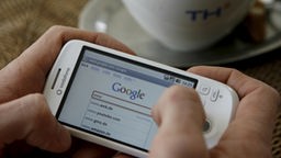 Ein Nutzer hält ein Android-Handy in einem Café in den Händen und sucht im Internet nach Informationen