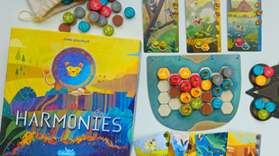 Die Spielschachtel von "Harmonies" zeigt einen bunten Löwen, daneben ein Spielbrett mit Geländespielsteinen und farbenfrohe Tierkarten