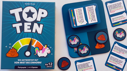 Die Spieleschachtel von "Top Ten" liegt neben einer Spielmatte aus Neopren, auf der ein Kartenstapel und Pokerchips mit Einhorn- und Kothaufen-Motiven liegen
