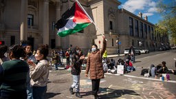 Eine pro-palästinensische Demonstrantin steht an einer Straßenkreuzung an der Yale University in New Haven und schwenkt eine palästinensische Flagge.