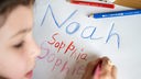 Ein Kind hat die Vornamen Noah, Sophia, allerdings mit einem doppelten "p", und Sophie mit Buntstiften auf ein Blatt geschrieben.