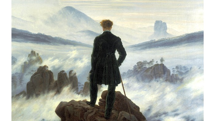 Ausschnitt des Geäldes "Wanderer über dem Nebelmeer" von Caspar David Friedrich, dass einen Menschen von hinten zeigt, der über eine neblige Hügellandschaft blickt.