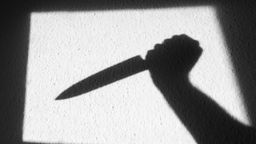 Foto eines Wandschattens von einer Hand mit Messer.