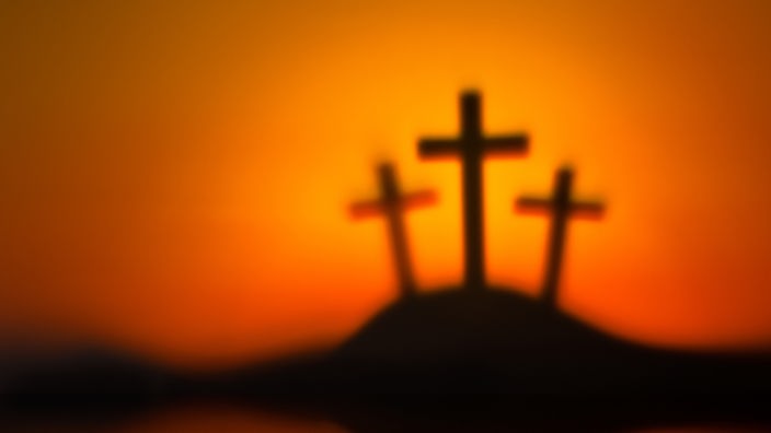 Drei schwarze Kreuze auf einem Hügel, der Hintergrund orange.