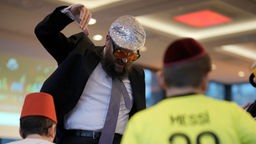 Rabbi Yehuda Teichtal tanzt mit übergroßer Brille und einer albernen Mütze am vergangenen Purimfest mit Kindern in Berlin