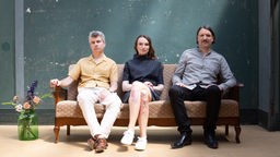 Foto des Trio Lange/Berweck/Lorenz auf einem Sofa vor einer grünen Wand.