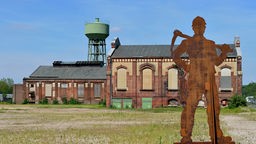 Das ehemaligen Zechengelände der Zeche Lohberg mit Industriegebäuden, einem Wasserturm und der Metallskulptur eines Bergarbeiters im Vordergrund.