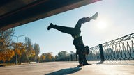 Symbolbild: Junger Breakdancer tanzt vor städtischen Hintergrund mit akrobatische Stunts.