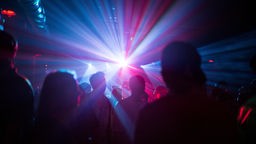 Die Silhouetten von Menschen werden von bunten Lichtern in einem Nachtclub beleuchtet.