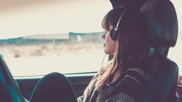 Eine june Frau sitzt in einem Auto und hört Musik, während sie aus dem Fenster blickt.