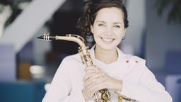 Asya Fateyeva hält lächelnd ihr Saxophon.