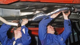 Automechaniker bauen im November 1987 in einer Autowerkstatt einen Abgas-Katalysator in einen Wagen ein.