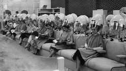 Frauen sitzen 1955 beim Friseur in einer Reihe unter der Trockenhaube 