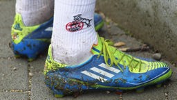 Ein Fußballer trägt dreckige Fußballschuhe und Socken mit einem 1. FC Köln-Emblem