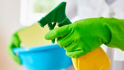 Hände von Reinigungskraft mit Handschuhen und Glasreiniger zum Fenster putzen