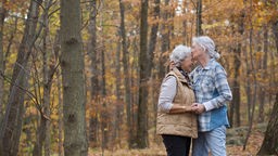 Zwei ältere Frauen halten sich im Wald in den Armen und küssen sich