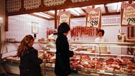 Aufnahme um 1975: Verkäuferin und Kunden an einer Fleischtheke in einer Metzgerei
