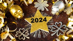 Die Jahreszahl 2024 steht auf einem goldenen Stern, der inmitten von Silvester-Deko liegt