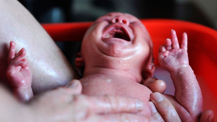 Neugeborenes Baby schreit und wird gebadet