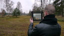Mann steht mit Tablet in leerer Landschaft in Bergen Belsen