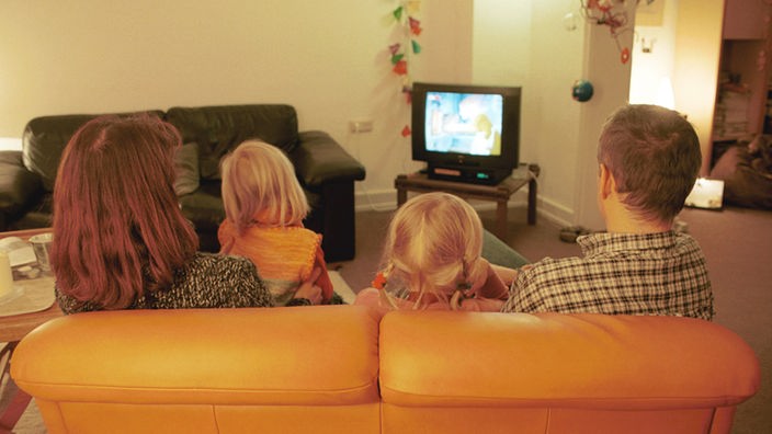 Eine vierköpfige Familie sitzt im Wohnzimmer auf der Couch und schaut fern