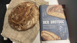 Ein Laib Brot ("Artisan") mit dem Backbuch von Björn Hollensteiner