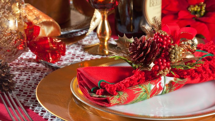 Ein gedeckter Tisch mit roter und goldener Weihnachtsdeko.