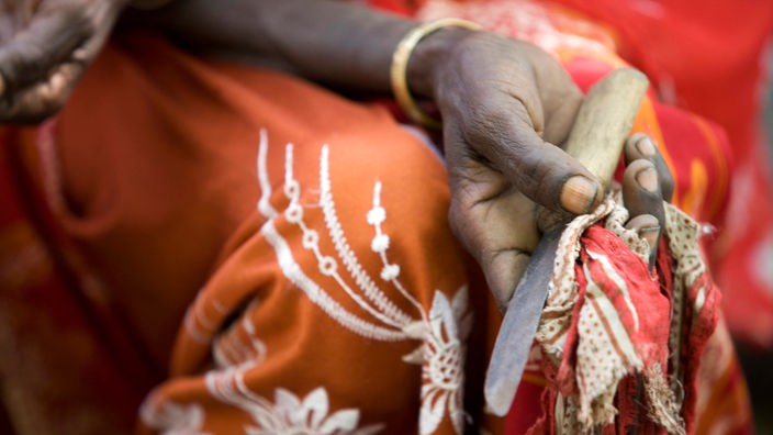 Das Beitragsbild WDR5 Dok5 "Perle – Der Weg zurück zur körperlichen Unversehrtheit" zeigt eine ehemalige Beschneiderin die ein rostiges Messer in der Hand hält.
